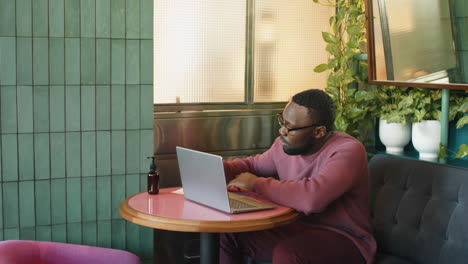 Hombre-Afroamericano-Usando-Laptop-Y-Tomando-Notas-En-El-Café